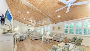 Ein geräumiges Wohnzimmer mit Holzboden, Deckenventilator und großen Fenstern.