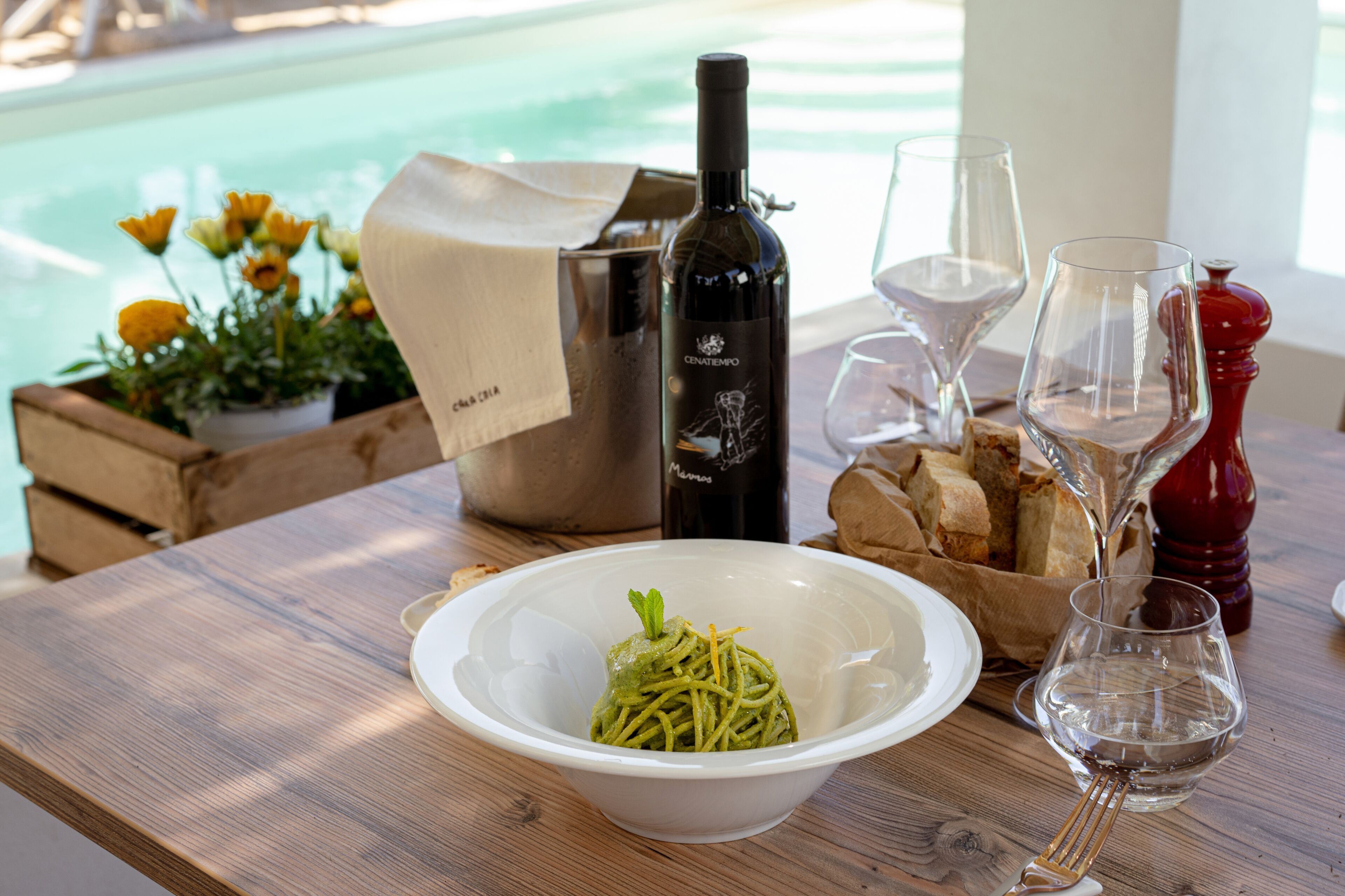 Una mesa de madera con un bol de pasta, una botella de vino, copas y pan.