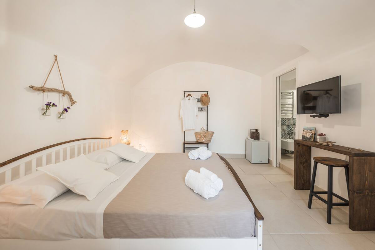 A bedroom with a bed, a desk, a TV, and a mirror.