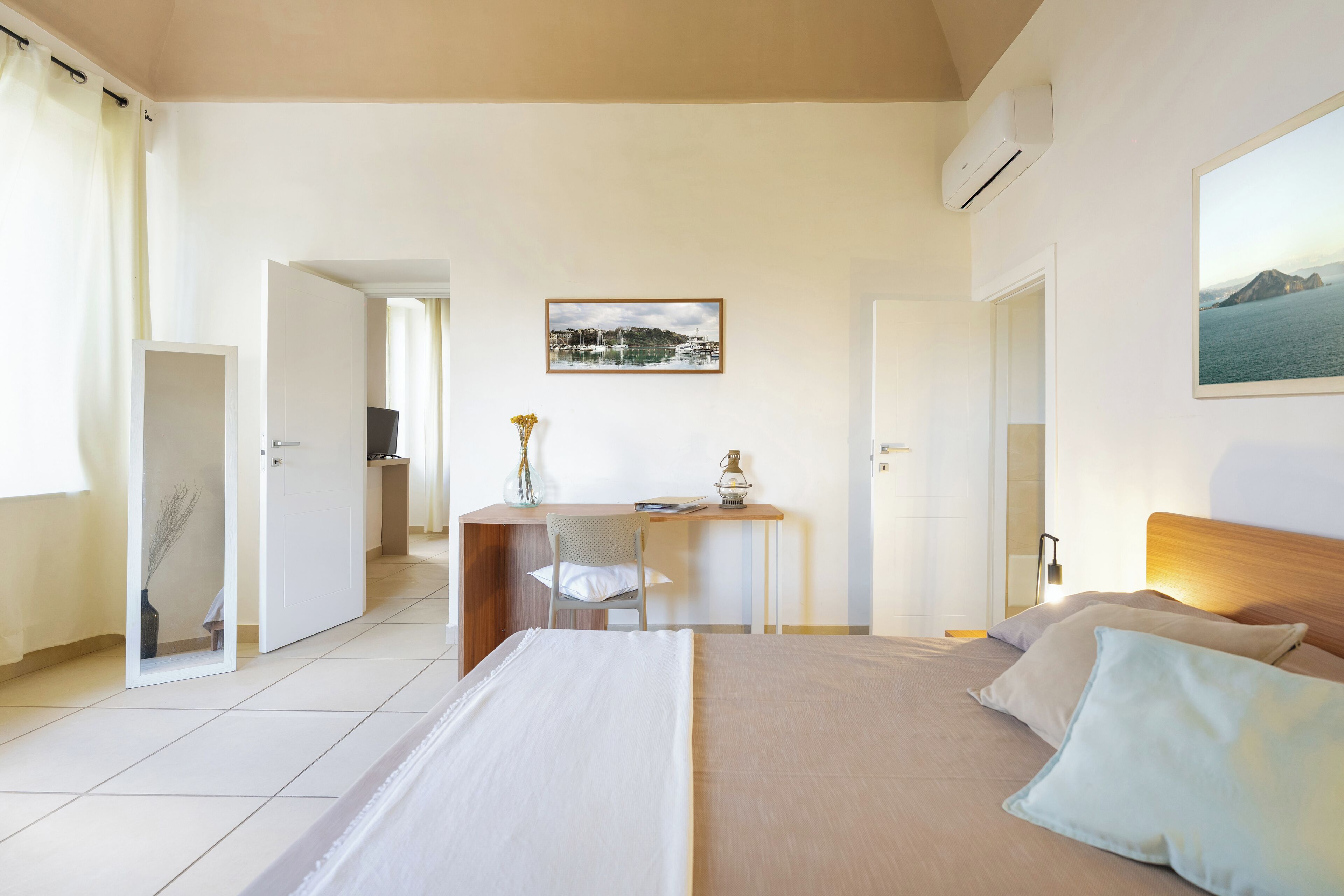 Habitación de hotel con cama, escritorio y silla. Hay un cuadro en la pared y un equipo de aire acondicionado.