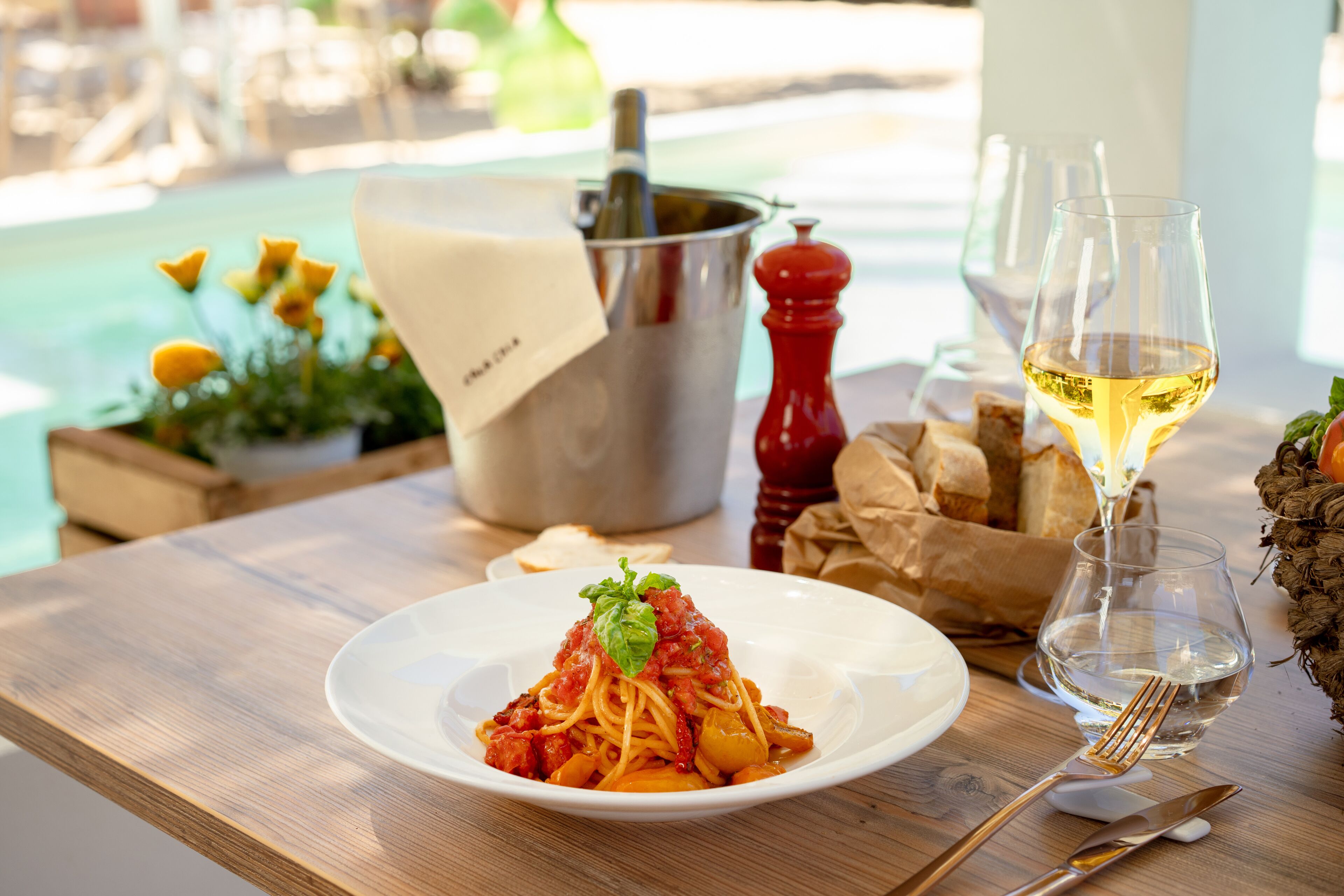 A wooden table with a plate of spaghetti, a wine glass, and a salt shaker.