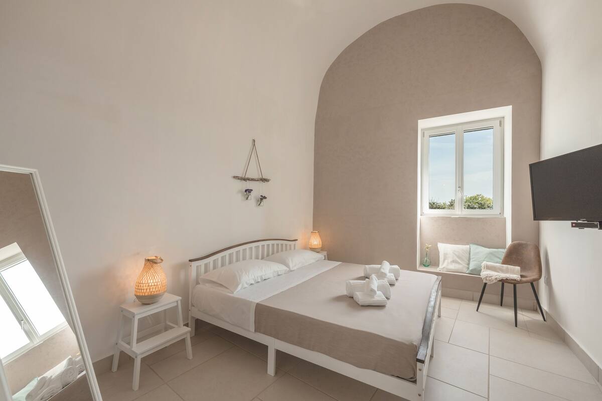 A bedroom with a bed, bedside table, lamp, chair, and a TV mounted on the wall.