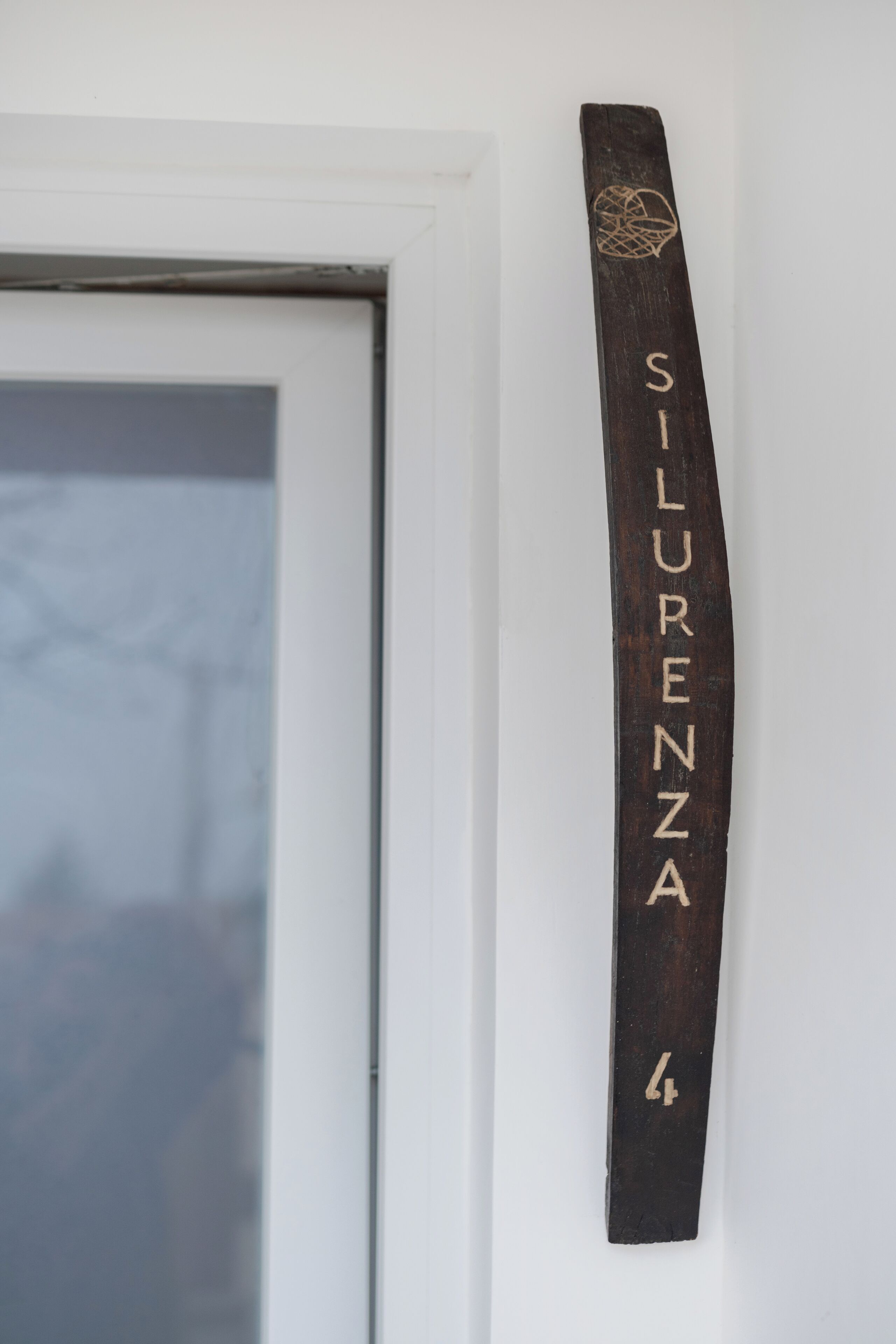 A wooden plaque with the inscription "SILURENZA" mounted on a white wall.