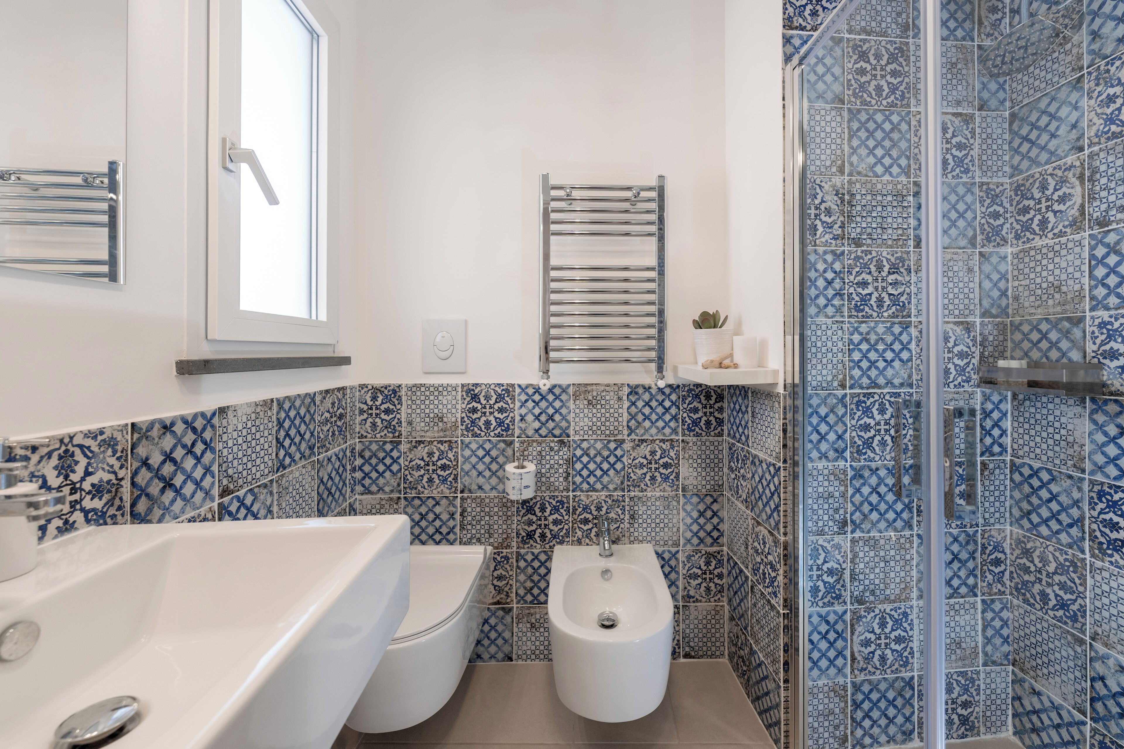 Bagno con lavandino bianco, toilette, bidet e zona doccia con piastrelle a motivi blu.