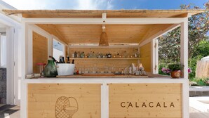 A wooden bar with shelves of bottles and glasses, a hanging light fixture, and a sign that reads "CALACALA". - Calacala rooms, restaurant & farm experience (Procida)