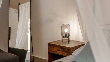 Un dormitorio con cama, mesita de noche con lámpara, espejo y una silla.