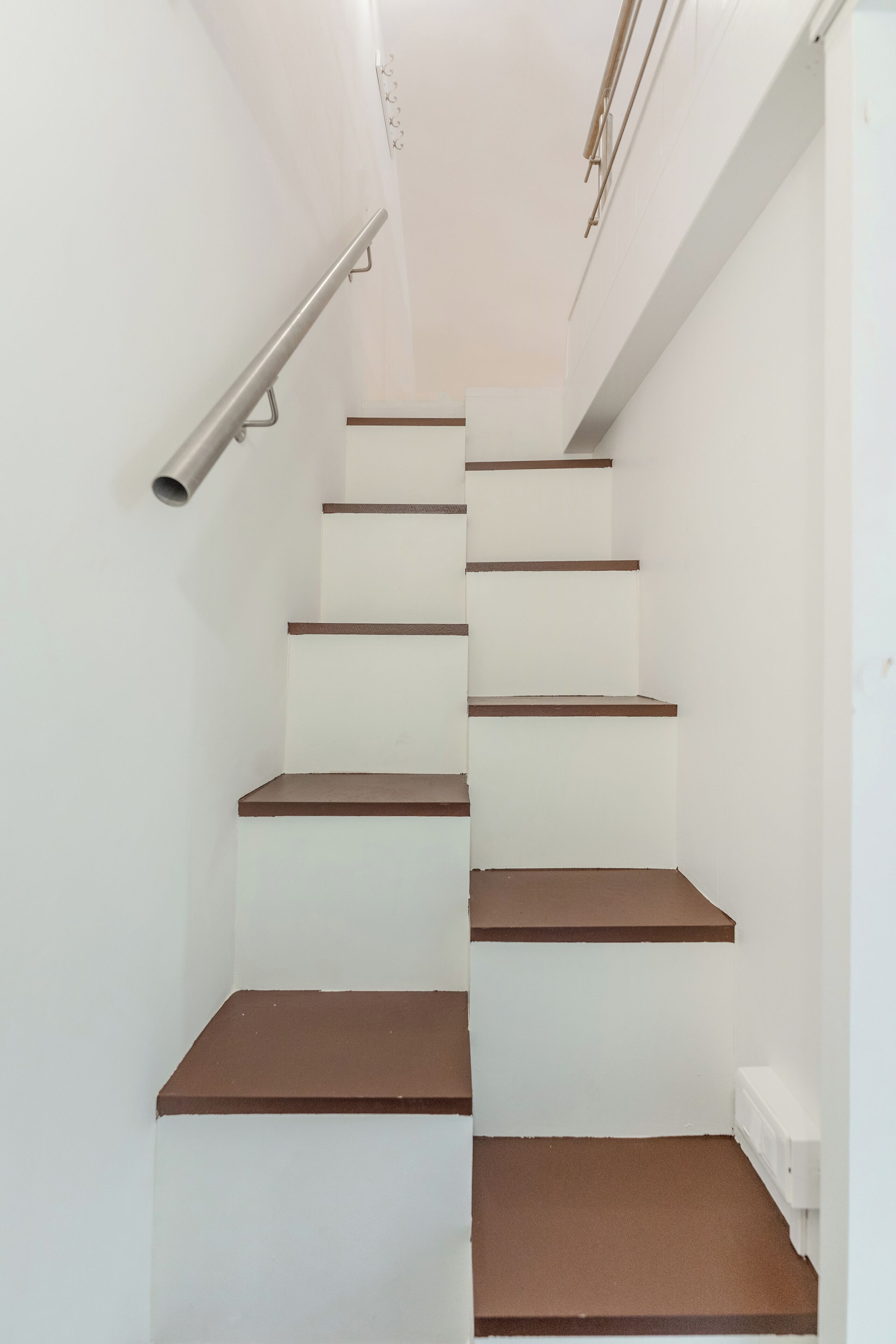 A staircase with white walls and brown steps.