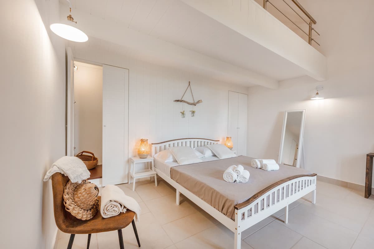 A bedroom with a bed, bedside tables, a chair, a mirror, and a hanging light fixture.