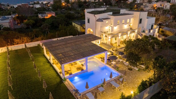 A modern villa with a swimming pool, outdoor seating, and a view of the city at dusk. - Calacala rooms, restaurant & farm experience (Procida)