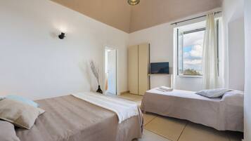 Una habitación de hotel con dos camas, un televisor, una ventana con cortinas y un jarrón con ramas.
