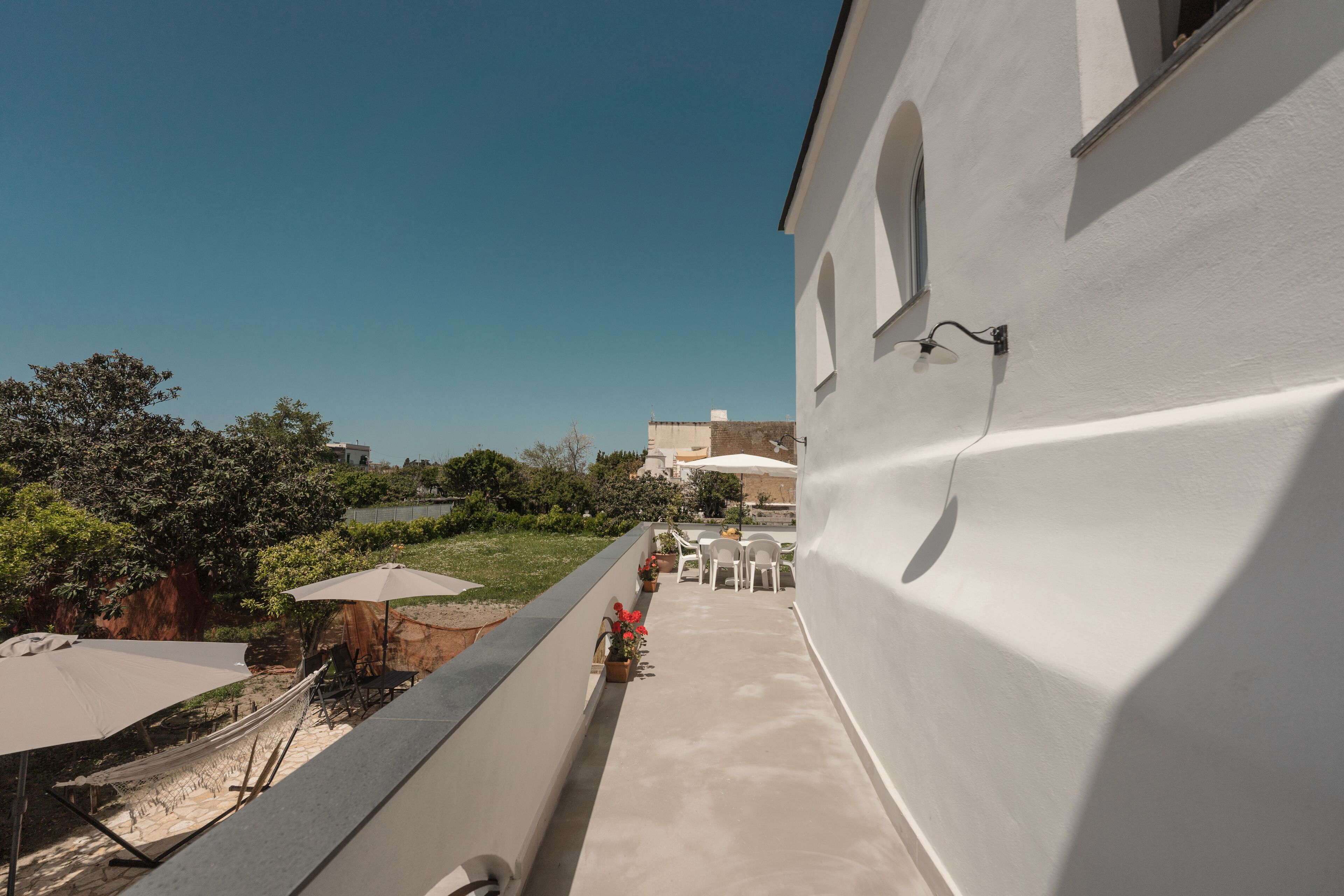 Un balcon avec des meubles d’extérieur, un bâtiment blanc et de la verdure en arrière-plan.