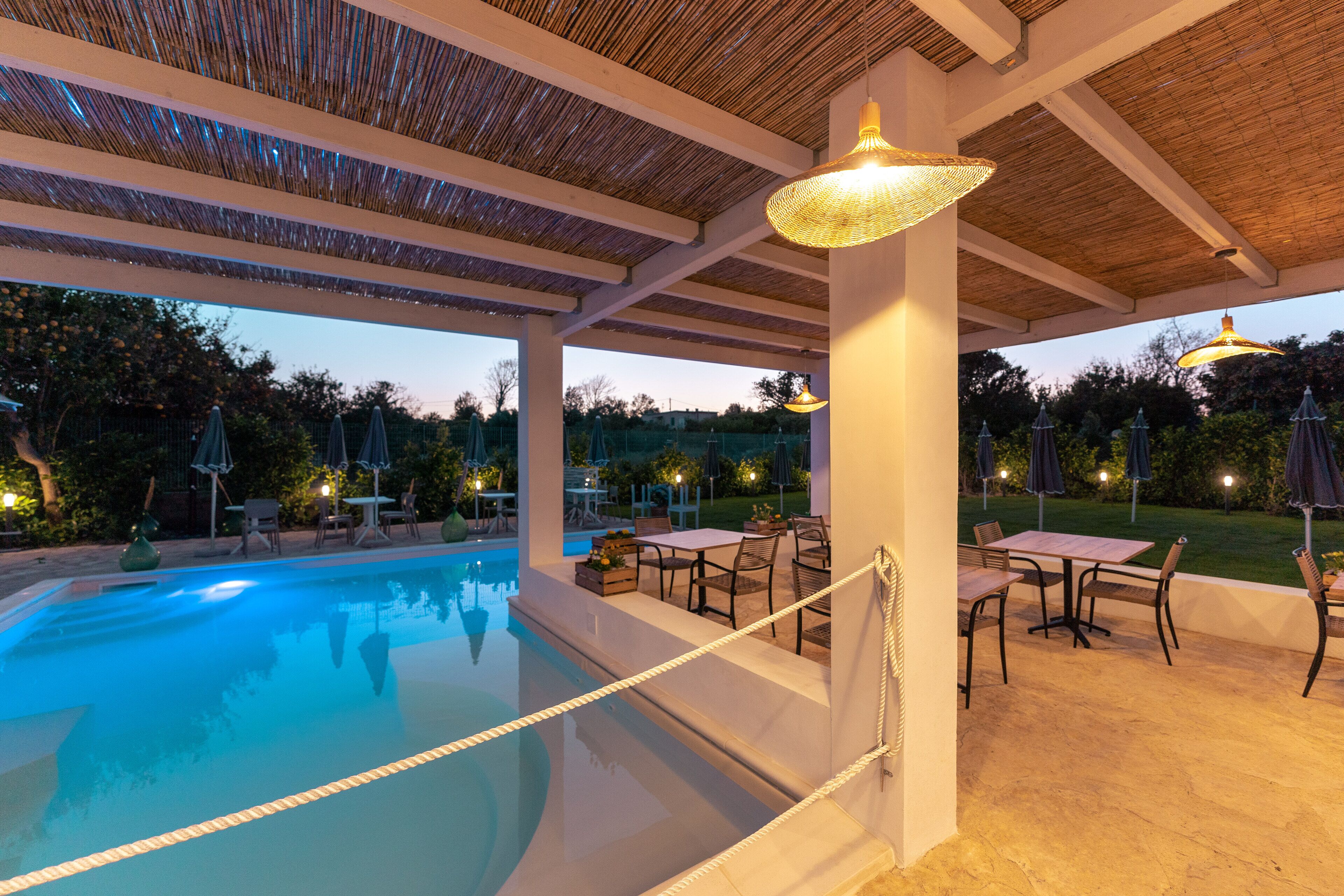 An outdoor pool area with a covered patio, tables, and chairs.