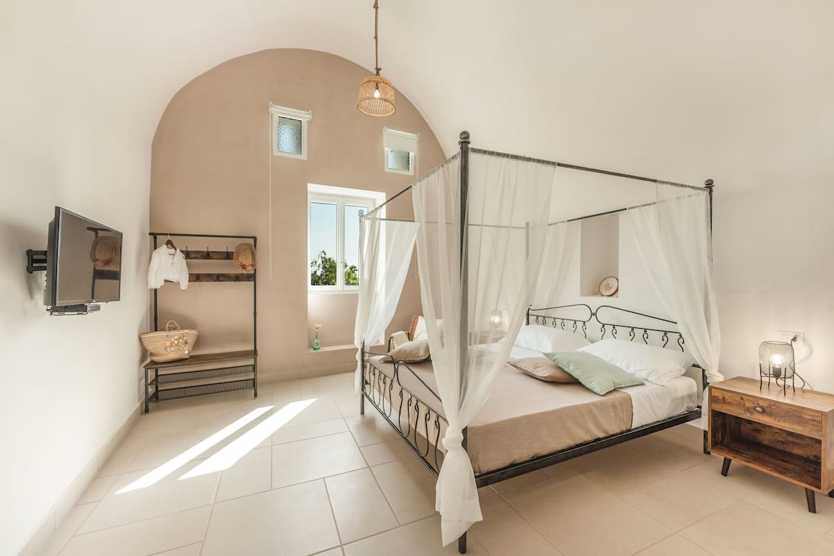 A bedroom with a four-poster bed, a bedside table, a TV, a window, and a wall-mounted shelf.