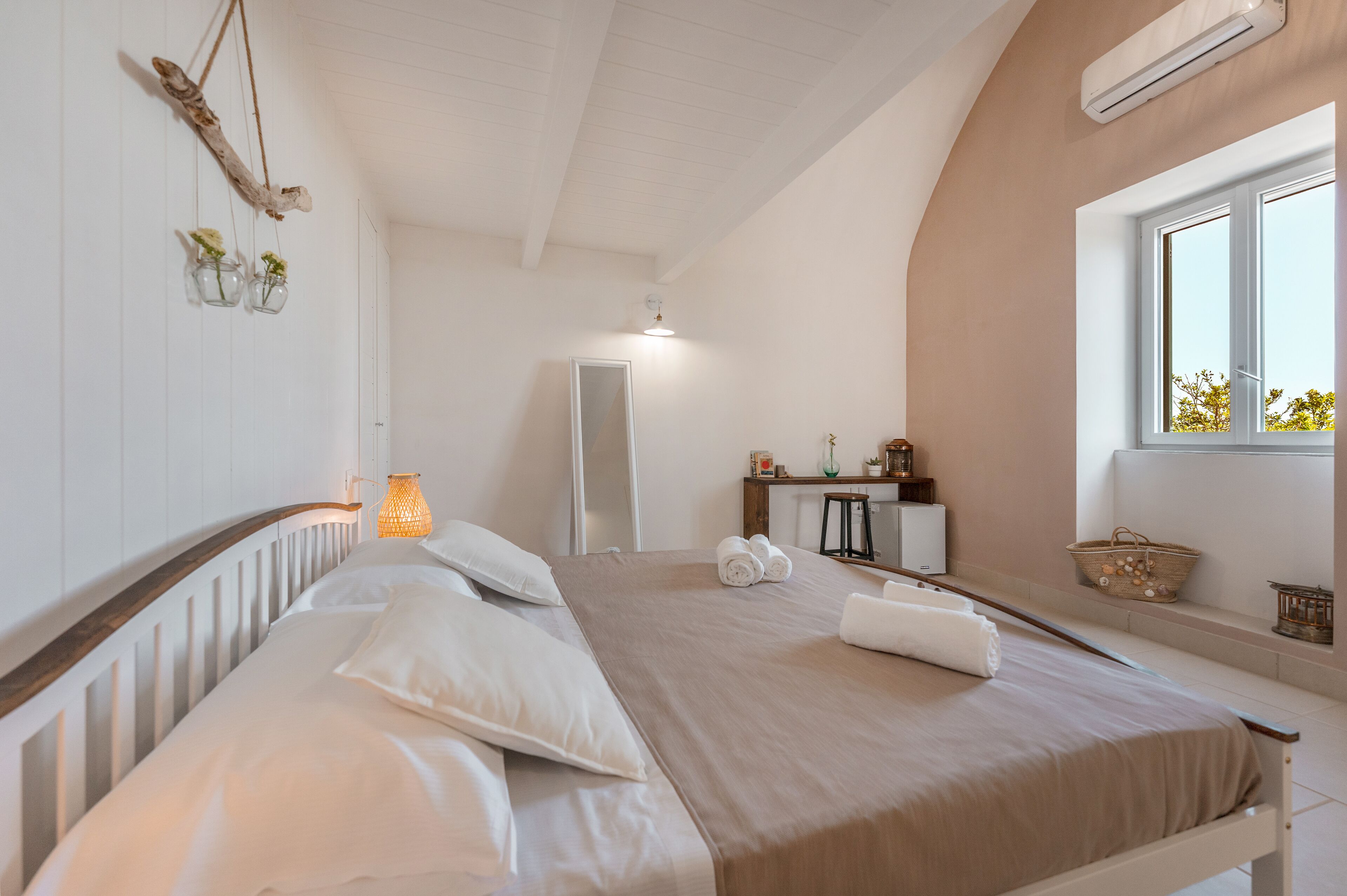 Un dormitorio con cama, mesita de noche, espejo y ventana.