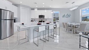 A modern kitchen with stainless steel appliances, white cabinetry, and a central island with bar stools. - Private Pool- Canal Front- Outdoor Bar- 5BR Sunsational Sunsets (Fort Myers Beach)