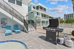 Zona de piscina con una parrilla, sillas de descanso y una piscina con borde de azulejos.