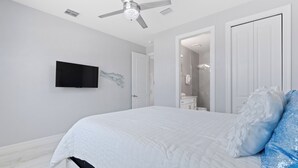 A bedroom with a bed, a ceiling fan, a TV, and a bathroom visible through an open door. - Private Pool- Canal Front- Outdoor Bar- 5BR Sunsational Sunsets (Fort Myers Beach)