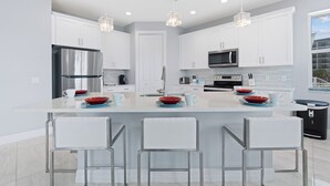 Una cocina moderna con muebles blancos, electrodomésticos de acero inoxidable y una isla central con taburetes de bar.