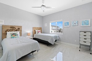 Un dormitorio con dos camas, ventilador de techo, ventana con vistas y obras de arte en las paredes.