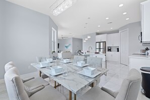 Een moderne eetruimte met een marmeren tafel en stoelen, een keuken met witte kasten, en een plafond met inbouwspots.