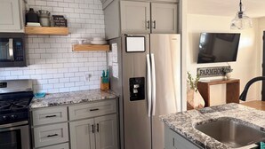 A kitchen with white tiled backsplash, stainless steel appliances, and a farmhouse sign. - Farmhouse - Centrally Located in Great Bend, Gas Firepit and Pet Friendly Yard (Great Bend)