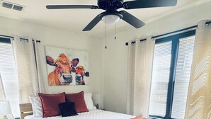 A bedroom with a bed, a ceiling fan, a painting, and a window with curtains. - Farmhouse - Centrally Located in Great Bend, Gas Firepit and Pet Friendly Yard (Great Bend)