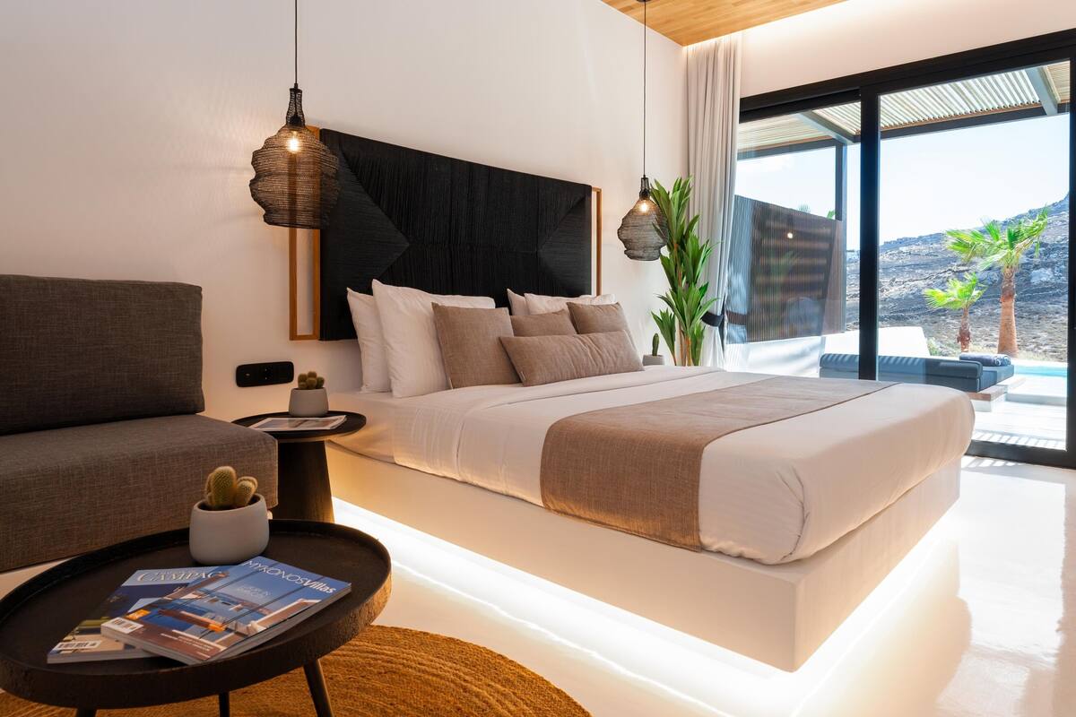 Ein modernes Schlafzimmer mit einem großen Bett, einem Sofa, einem Couchtisch und Blick ins Freie.
