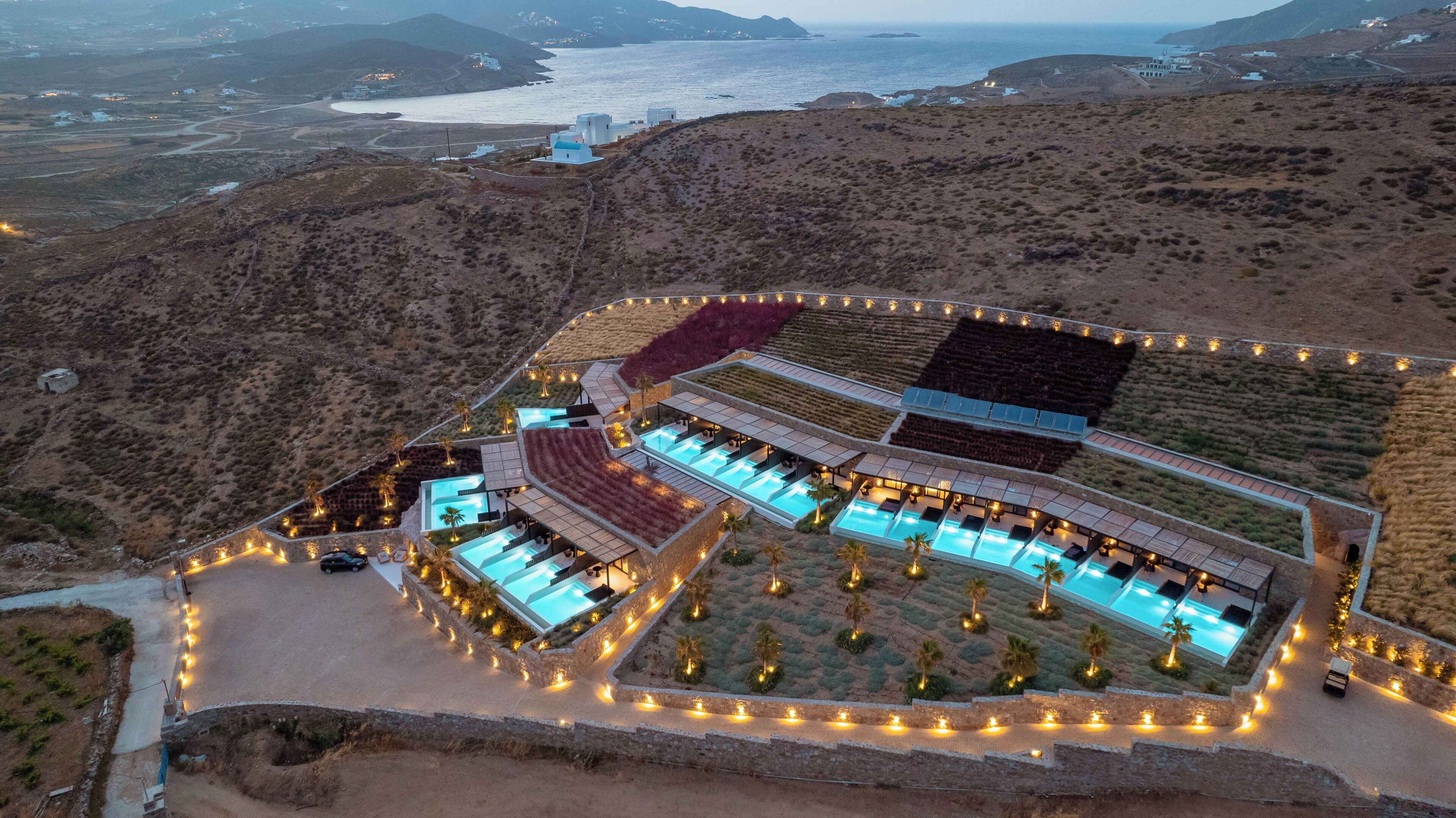 An aerial view of a resort with multiple swimming pools, a landscaped garden, and a coastal backdrop.