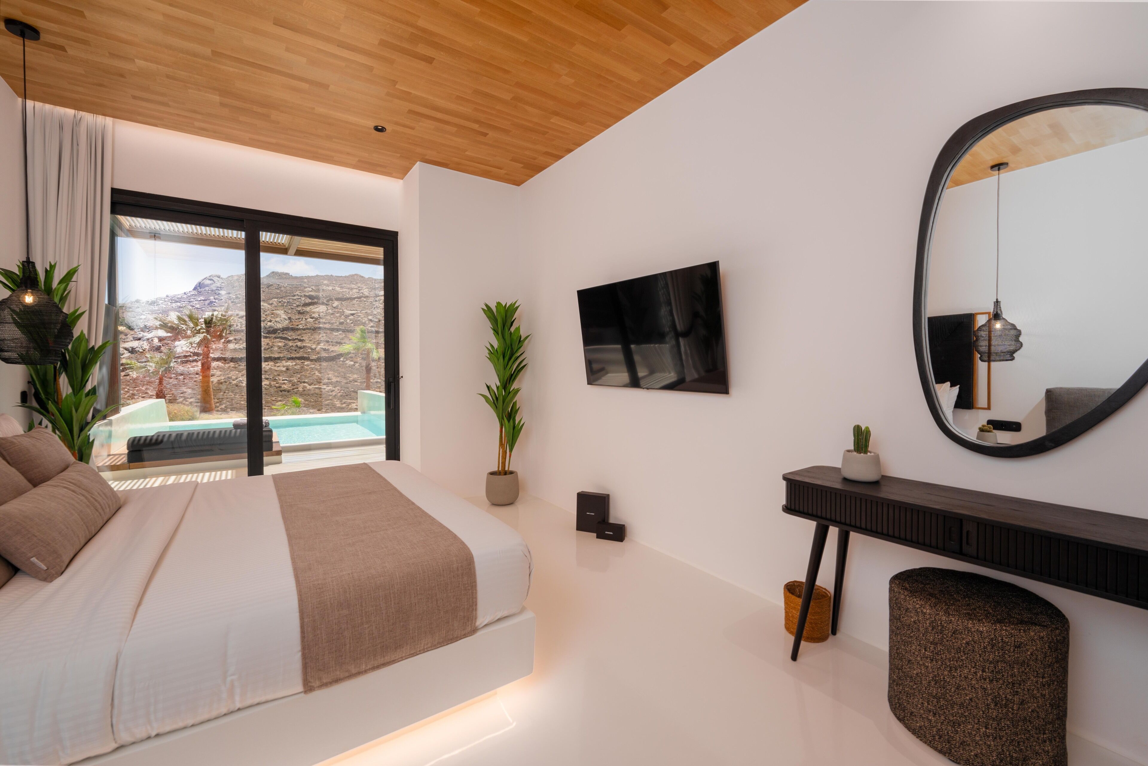 A modern bedroom with a large bed, a view of a mountainous landscape, a small pool, and a large mirror.