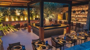 Un restaurante con barra, mesas dispuestas y un gran árbol como centro de decoración.