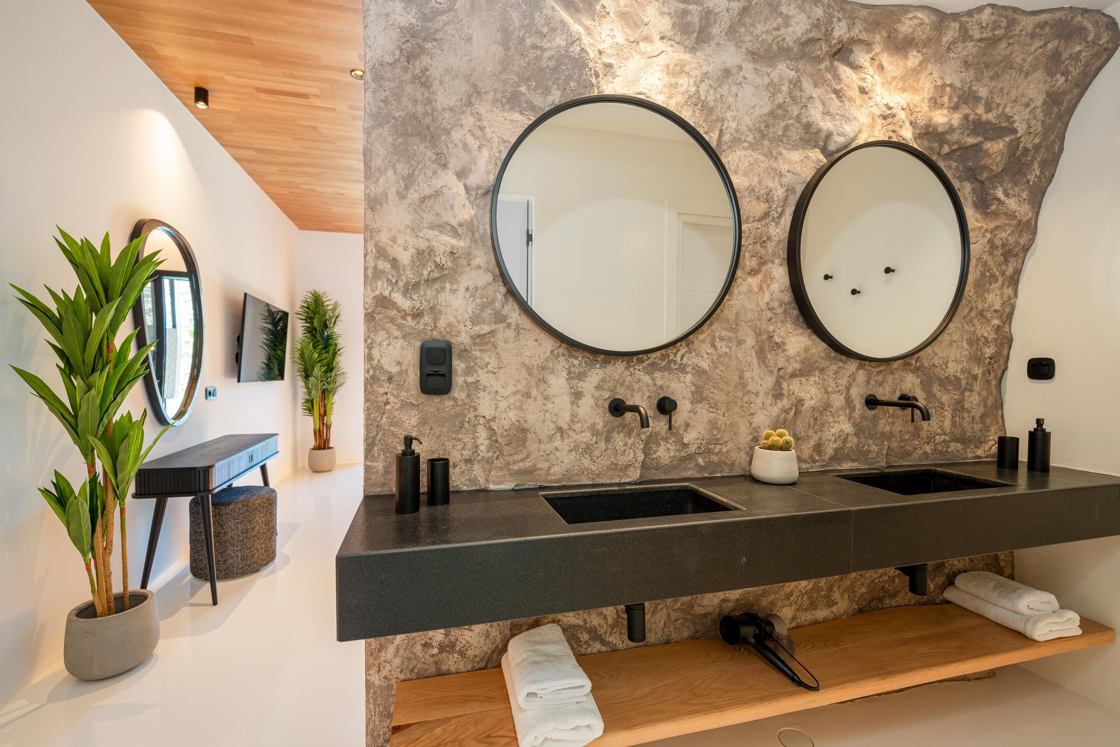 A modern bathroom with two sinks, a wooden bench, and a large mirror.