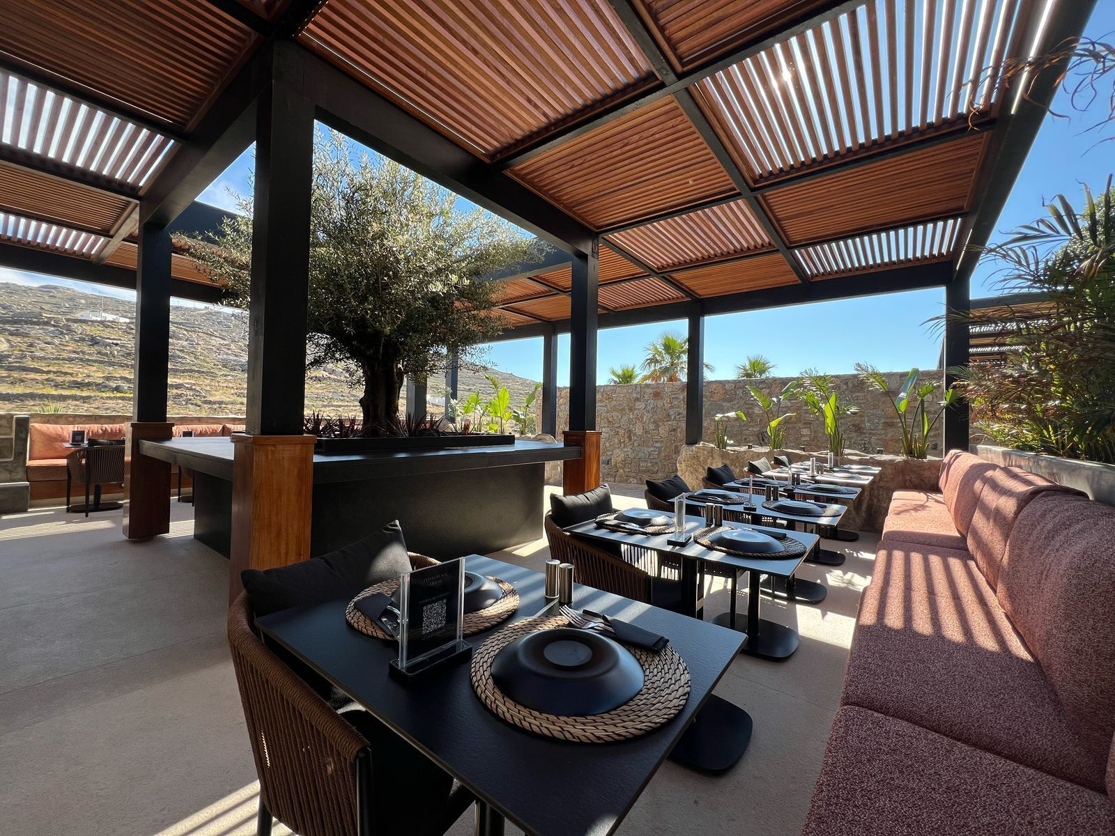 An outdoor dining area with multiple tables and chairs, a large tree, and a view of the surrounding landscape.