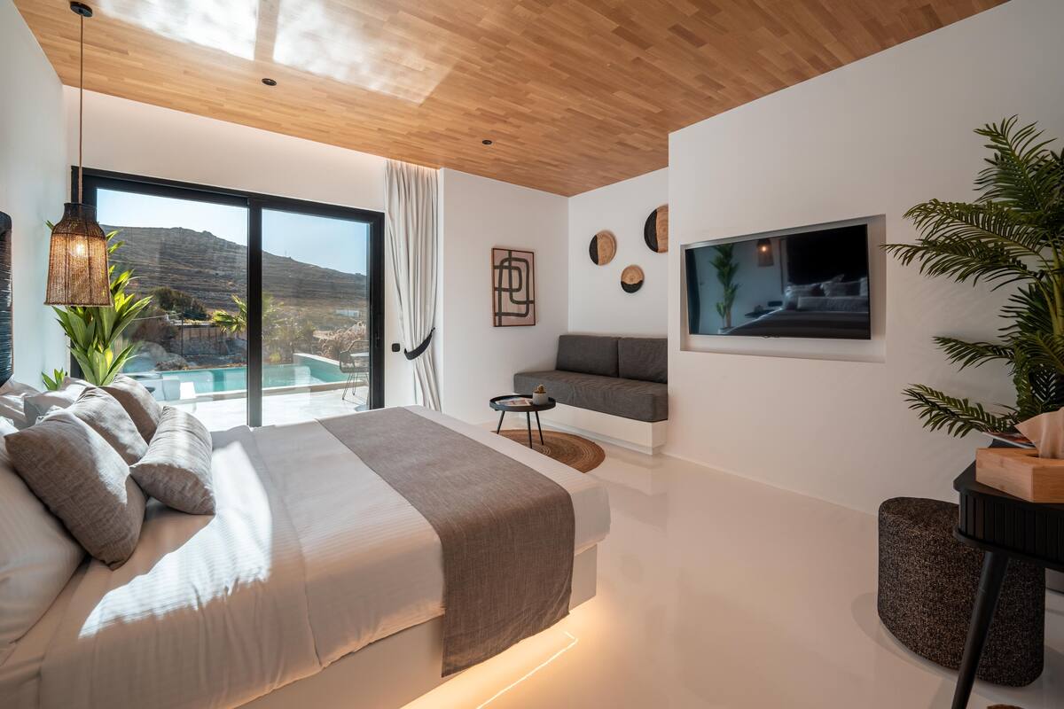 Ein modernes Schlafzimmer mit einem großen Bett, einem Fernseher und Blick auf eine Berglandschaft.