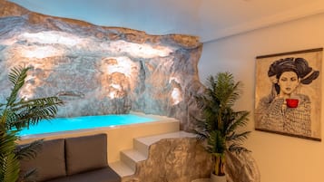 Un espacio de spa con una camilla de masaje, un rincón de descanso, una pared con textura rocosa y un elemento de agua.