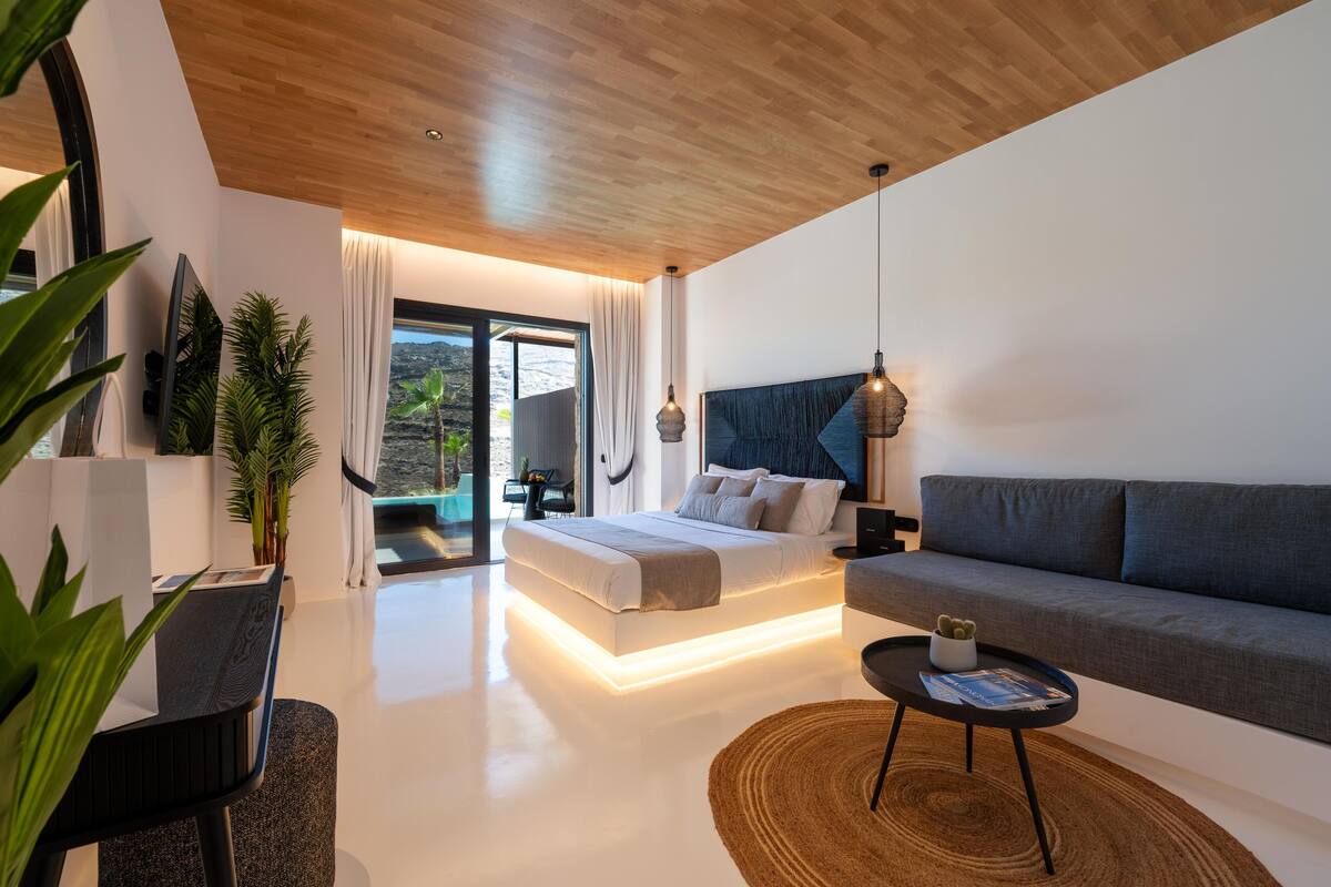 Ein modernes Schlafzimmer mit Bett, einer Couch, einem Esstisch und einem großen Fenster.