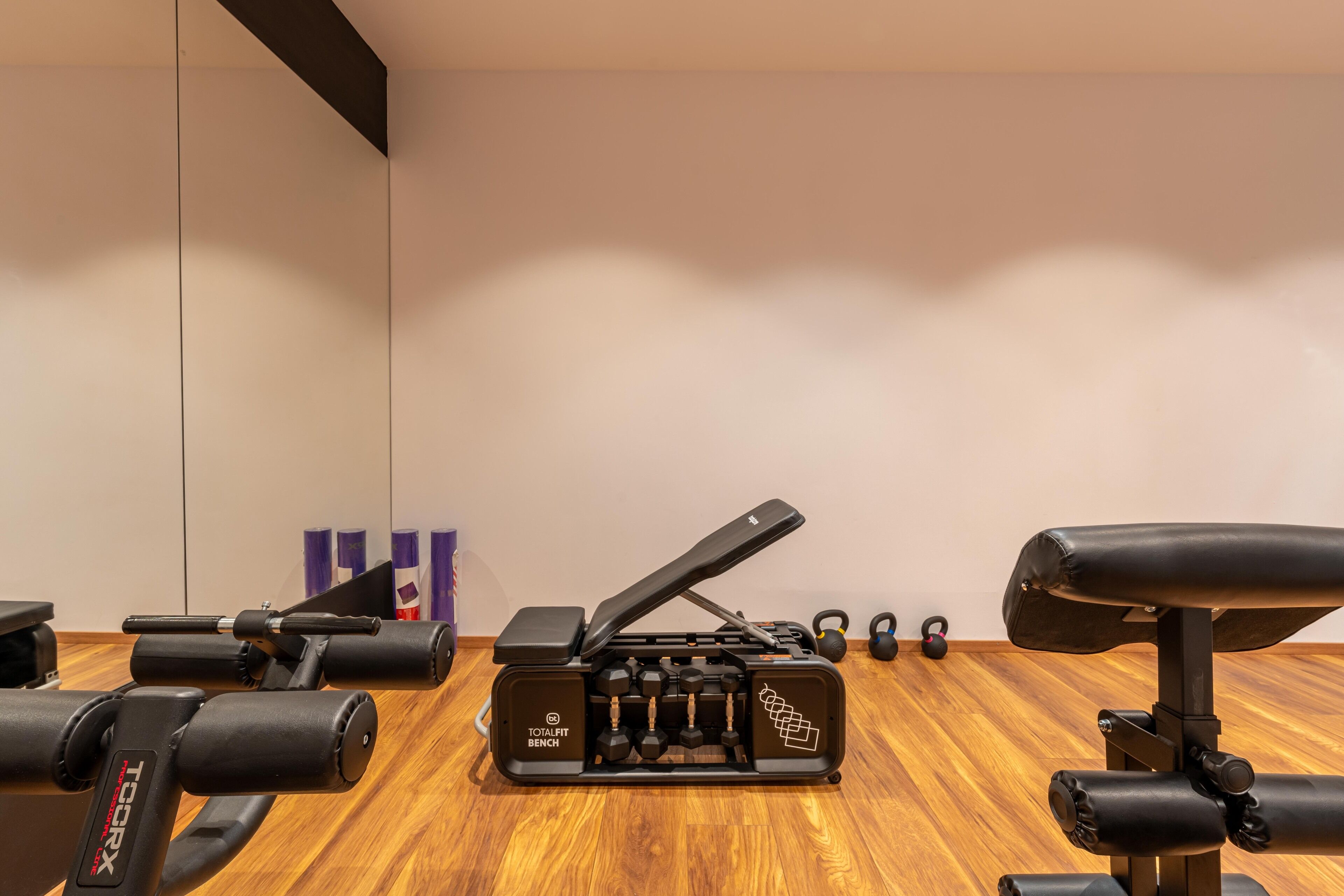 A gym with a wooden floor, a bench press, dumbbells, and kettlebells.