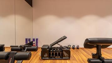 Uma academia com piso de madeira, aparelho de supino, halteres e kettlebells.