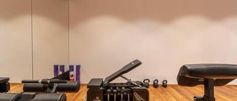 A gym with a wooden floor, a bench press, dumbbells, and kettlebells.