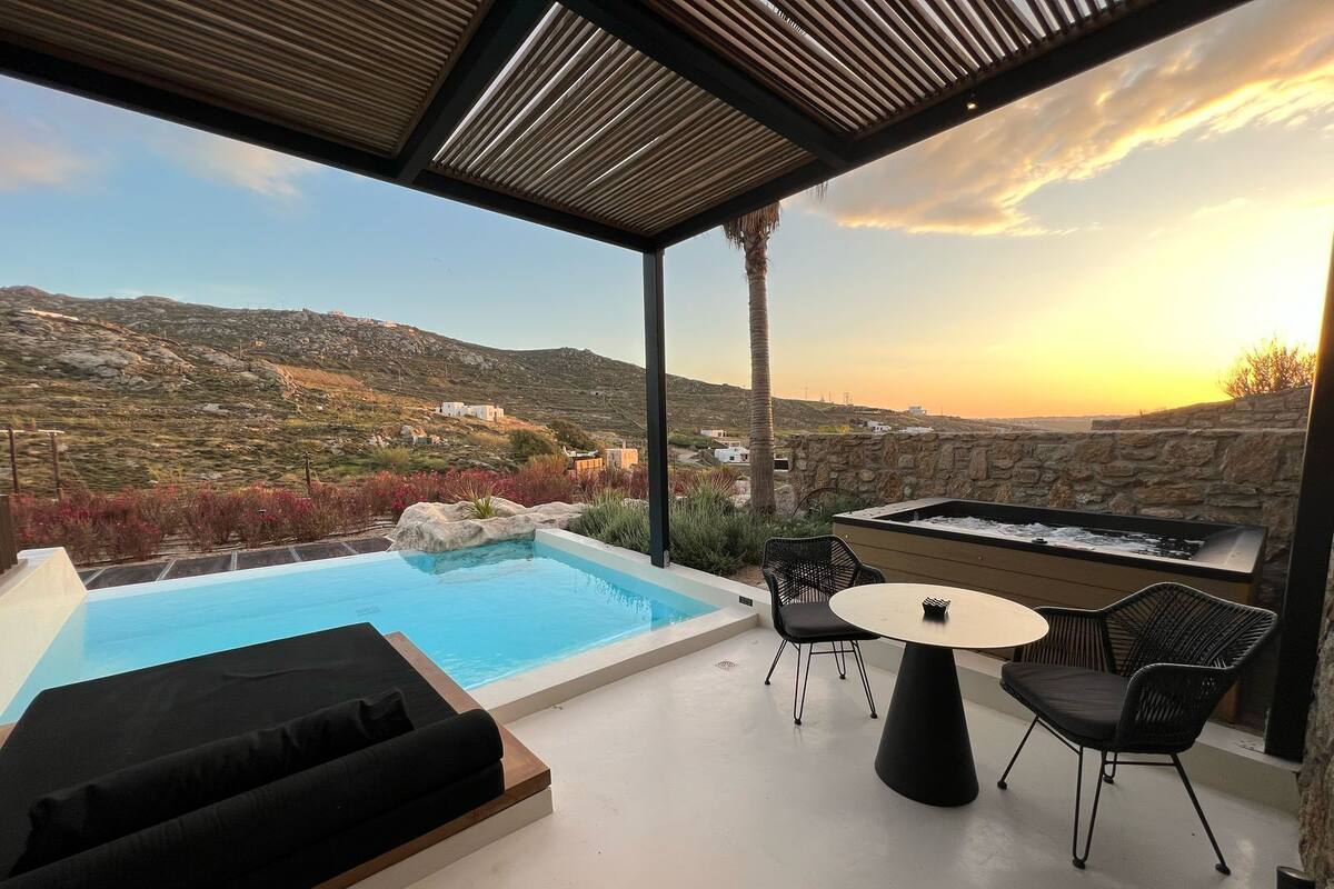 Ein Poolbereich auf dem Dach mit Blick auf die Landschaft, eine Sitzgelegenheit mit Tisch und Stühlen sowie eine Steinmauer.