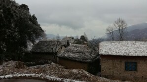 A rustic village with traditional thatched-roof houses, a stone building with a window, and a snow-covered landscape. - Water Ink Yuanyang Hotel Yuanyang (Yuanyang)