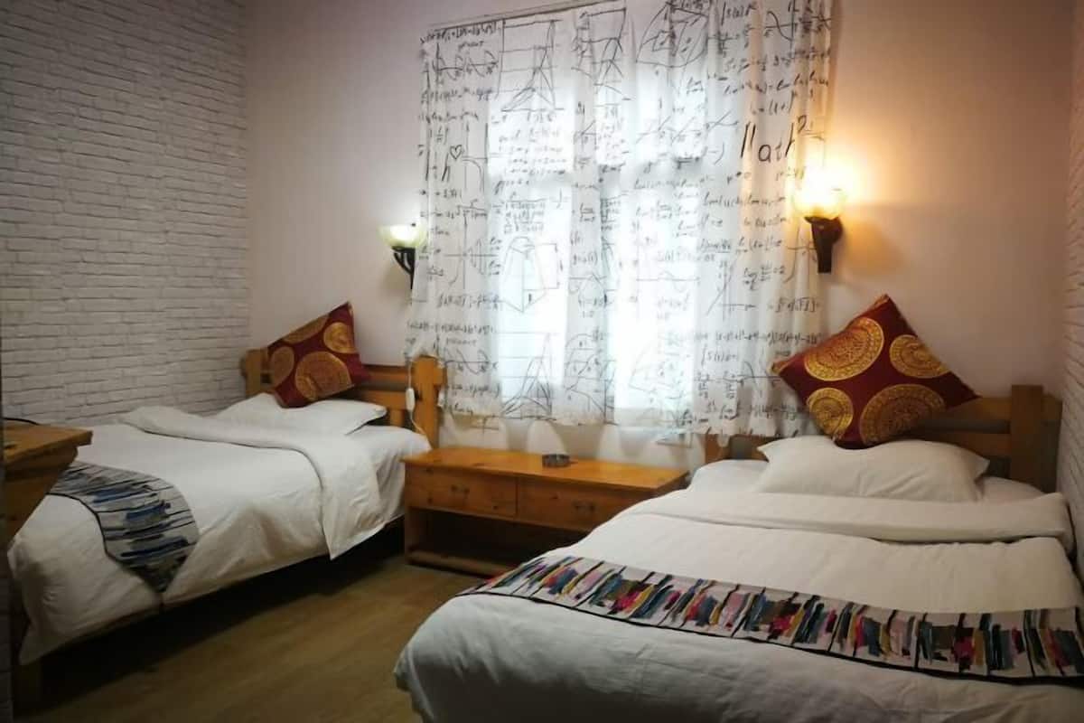 A room with two single beds, wooden headboards, a white brick wall, a window with a curtain featuring mathematical equations, and a nightstand with a lamp.