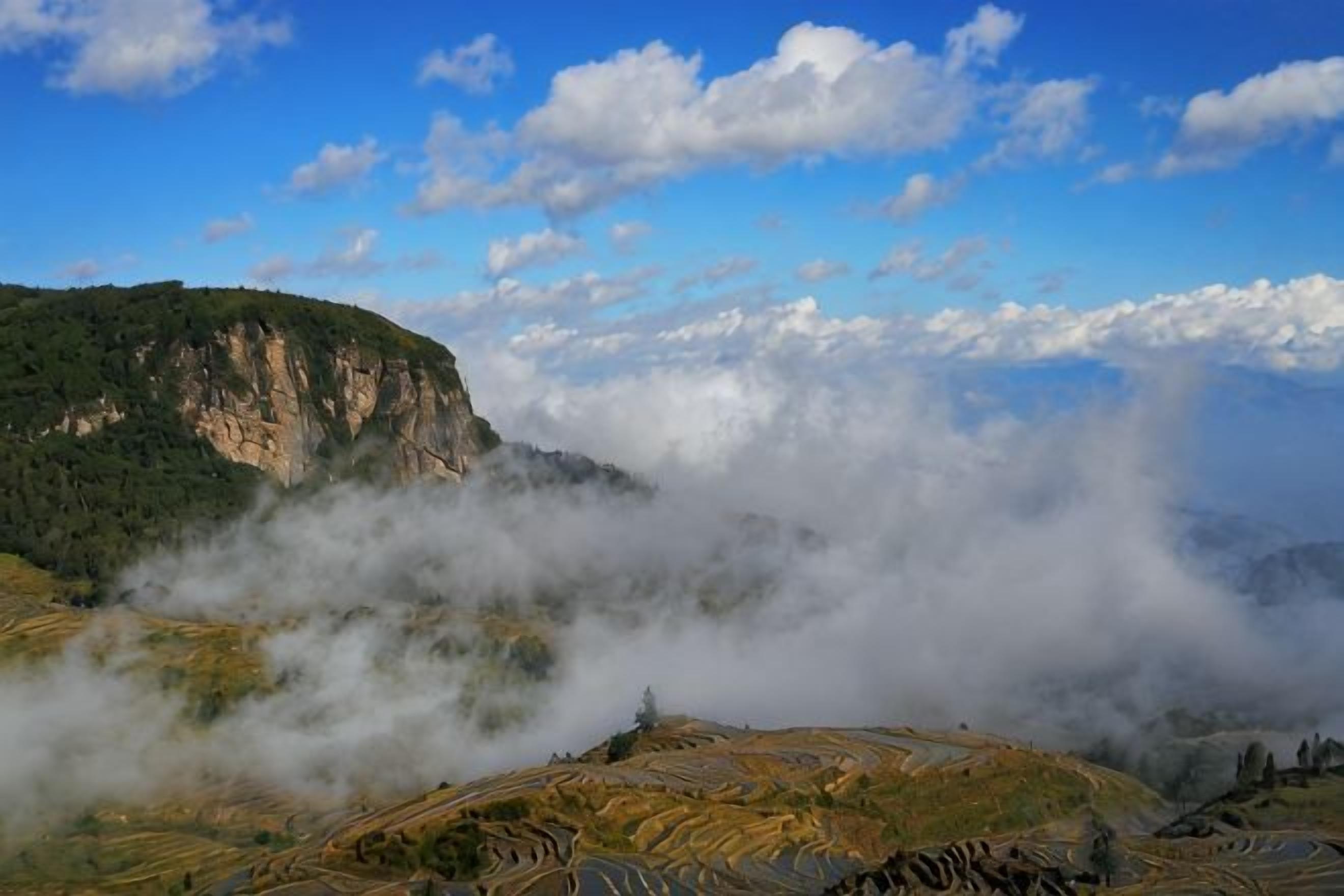 A mountainous landscape with terraced fields and a cliff.
