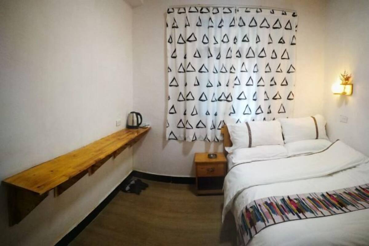 A bedroom with a bed, a wooden bench, a patterned curtain, and a small bedside table.