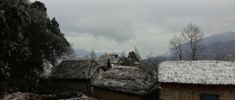 Un pueblo rural con casas de techo de paja tradicionales, un muro de piedra y montañas al fondo.