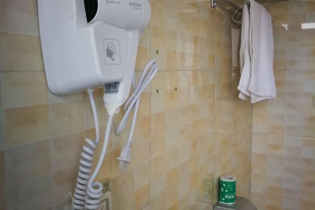 A bathroom with a hairdryer mounted on the wall, a towel hanging on a rack, and a toilet paper dispenser.