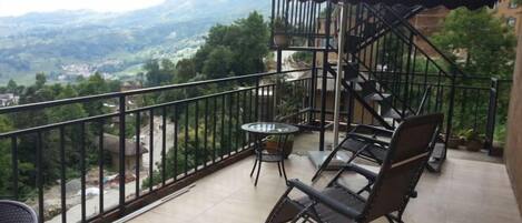 A balcony with a view of a mountainous landscape, a small round table, two chairs, and a staircase.
