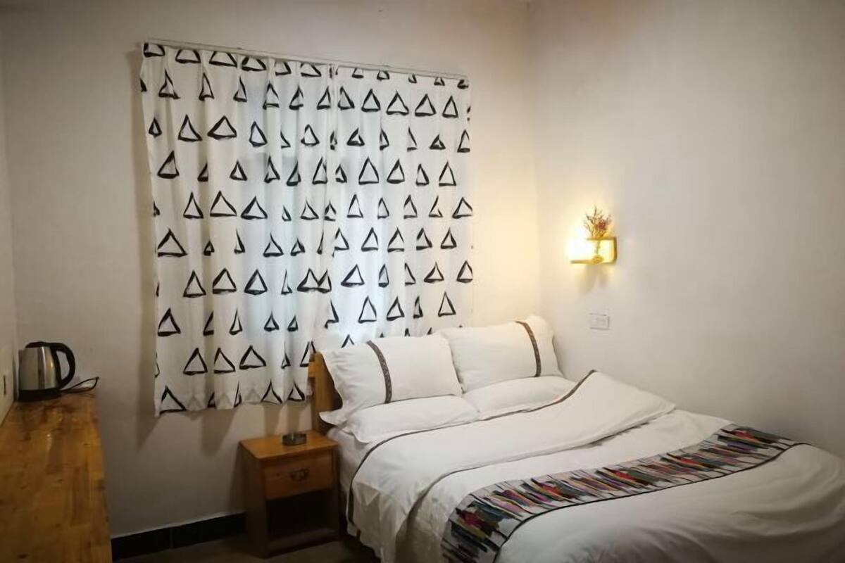 A bedroom with a bed, a nightstand, a lamp, and a kettle on a wooden table.