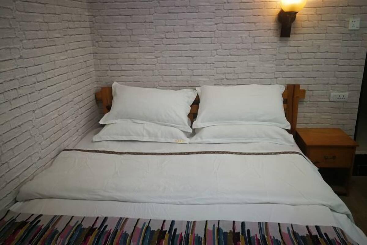 A bed with white bedding and a colorful striped blanket, a wooden headboard, and a nightstand with a lamp.