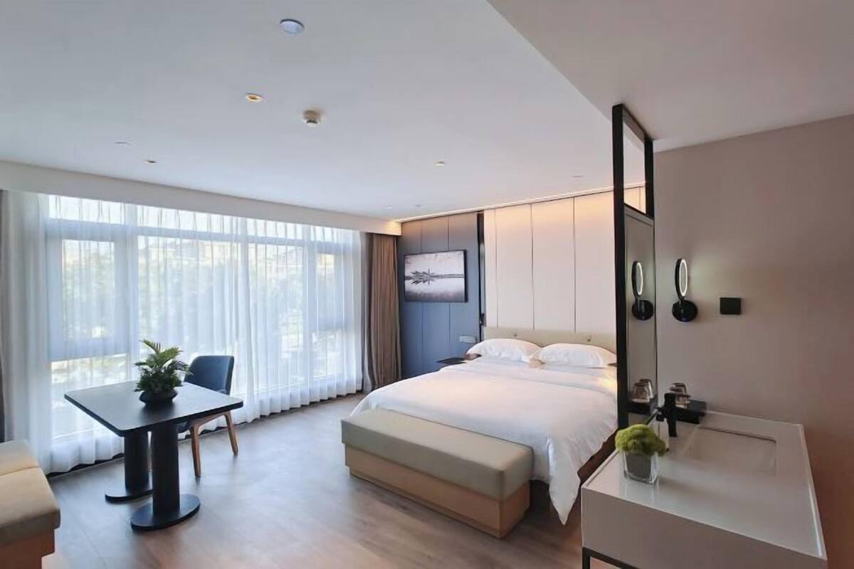 Una habitación de hotel moderna con cama, mesita de noche y un ventanal grande.