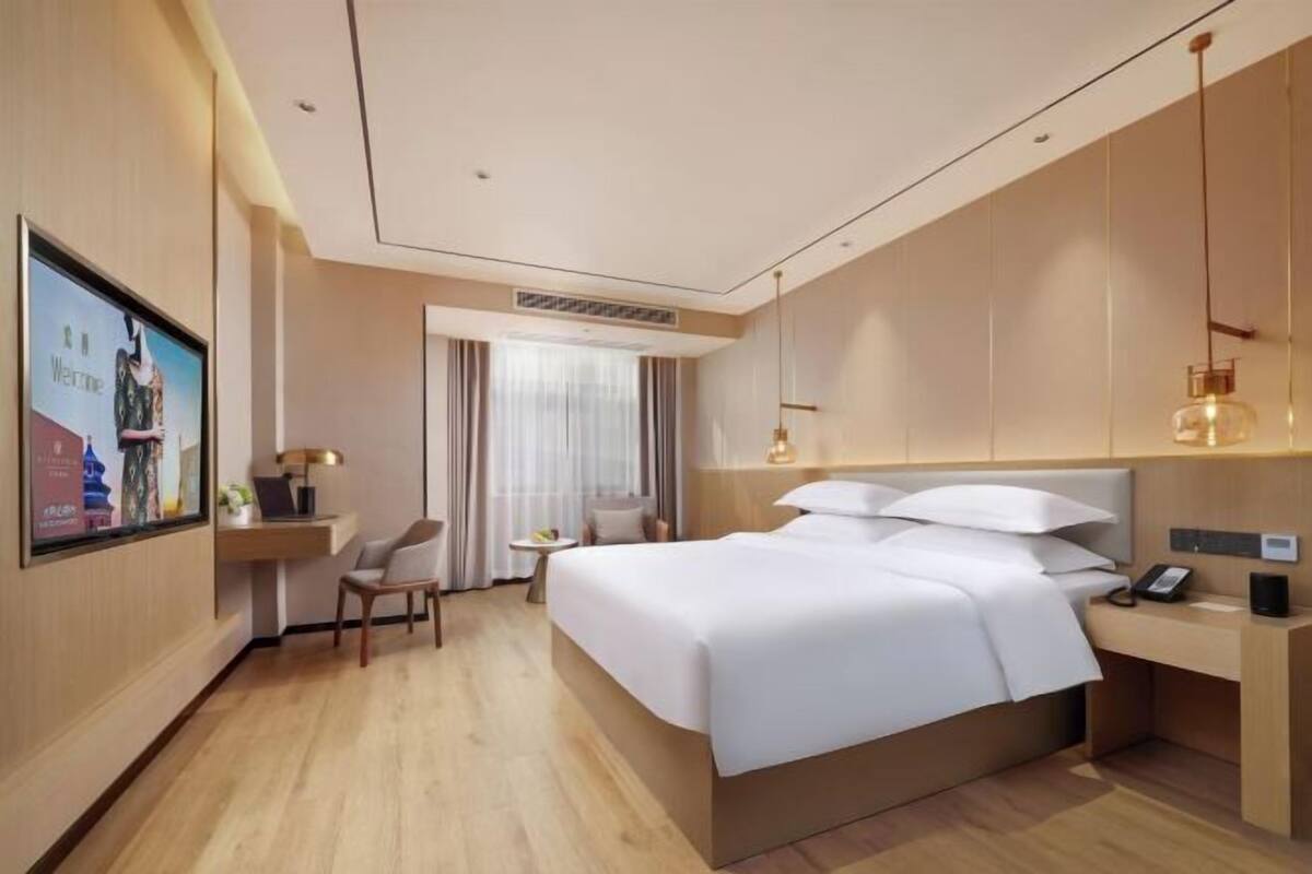 Una habitación de hotel moderna con una cama grande, un escritorio, una silla y un televisor en la pared.